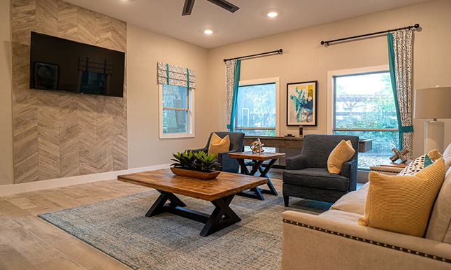 A living room furnished with two couches, a table, a carpet, and a TV on the wall
