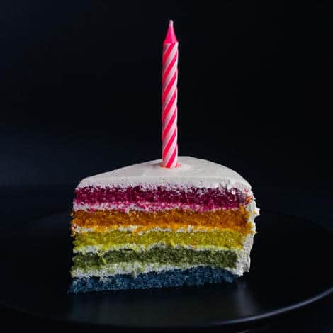 A single slice of birthday cake with an unlit pink candle sticking out of the top